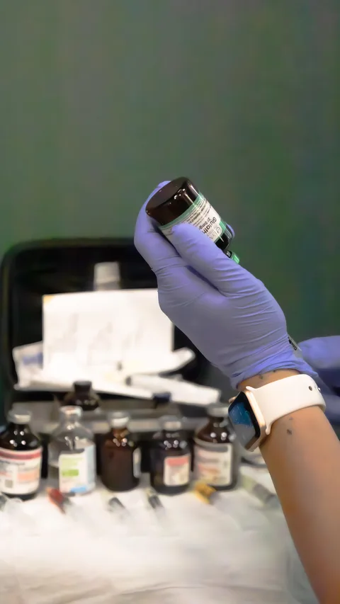 A nurse's gloved hand holding up a vial over the DrpIV+ kit