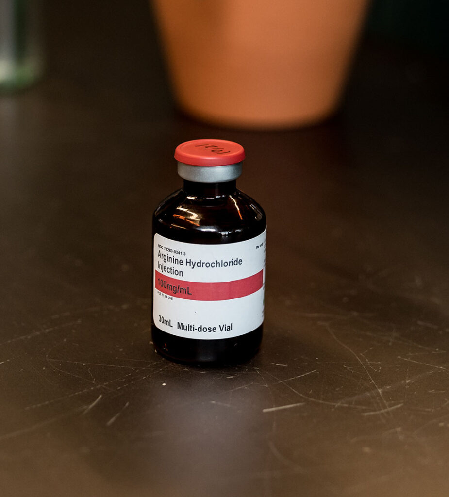 Arginine Hydrocholoride in Vial on a brown table with an orange pot in the background